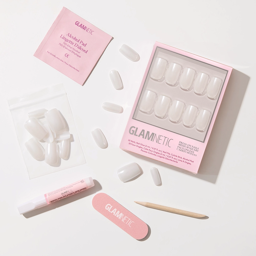 The Bailey vegan nail kit by glamnetic includes medium square semi-transparent nails, a pink nail file, wooden cuticle stick, glue tube, alcohol pad, spare nails in a bag, all in a pink glamnetic box on a white surface. - Product image