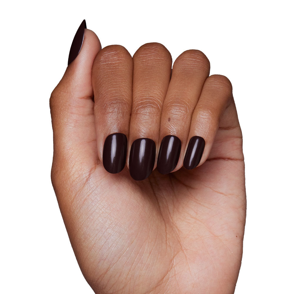 A hand with medium-brown skin displays the Bark Brown nail set by glamnetic, neatly manicured and painted in dark brown polish, shown against a white background. - Product image