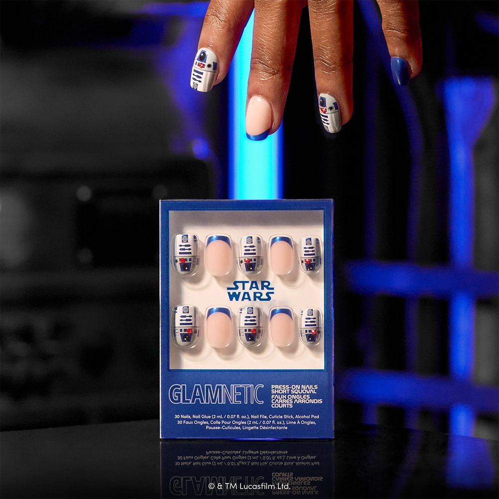 A hand with glamnetic Beep-Boop press-on nails, designed to look like R2-D2, hovers above a box labeled glamnetic Beep-Boop containing more matching short squoval press-on nails. Blue lighting glows in the background. - Product image