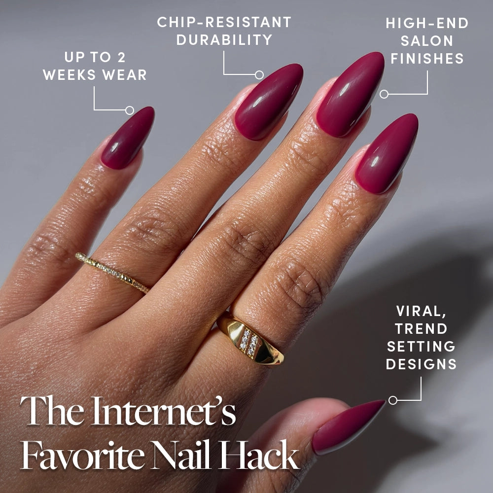 A hand with long, almond-shaped Berry Obsession nails by glamnetic showcases glossy maroon press-ons and chic gold rings. Enjoy up to 2 weeks wear, chip-resistant durability, salon finishes, and viral trendsetting designs. - Product image