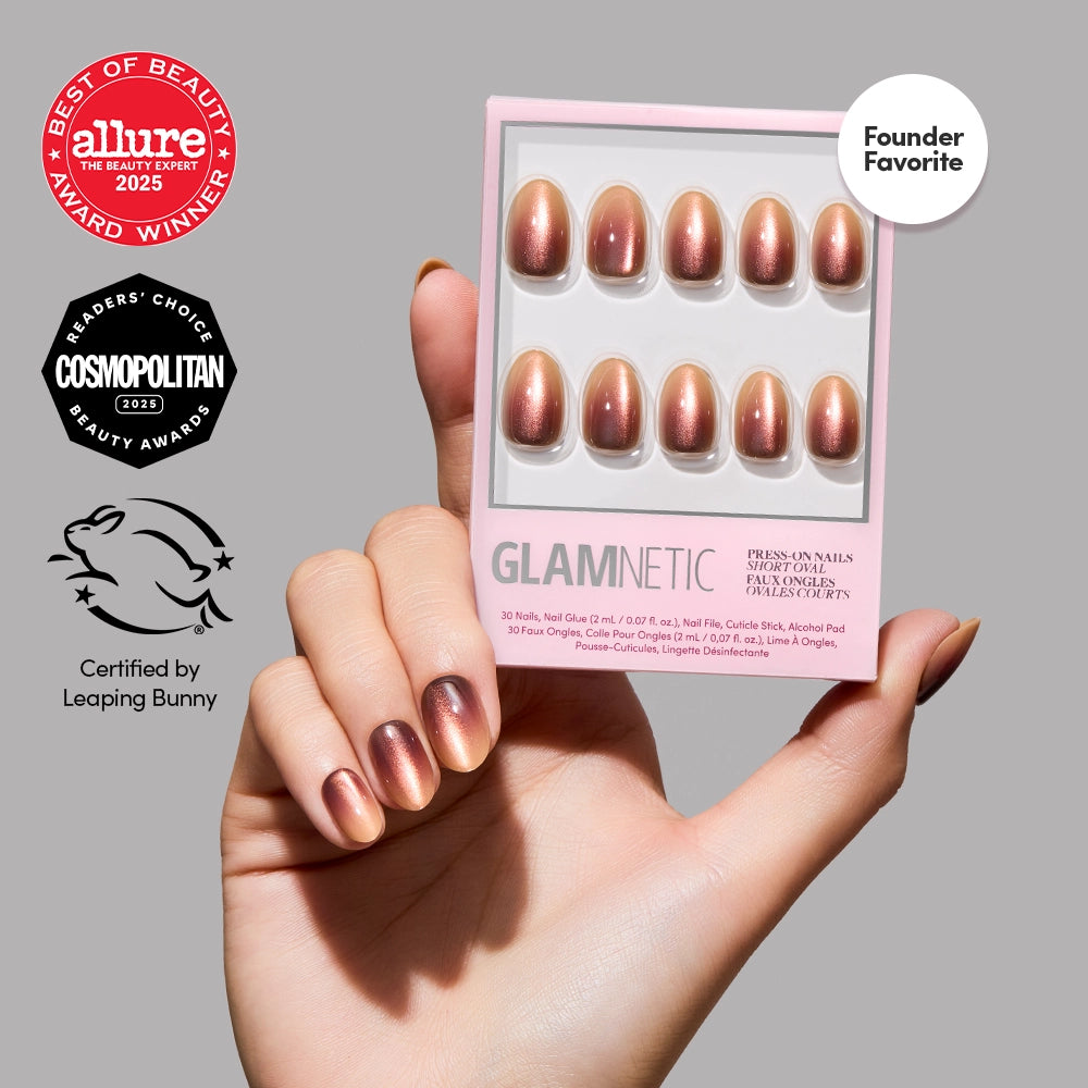 A hand with metallic rose gold velvet Bitter Orange press-on nails holds a box of glamnetic nails. Award badges from Allure, Cosmopolitan, and Leaping Bunny are displayed on a light gray background. - Product image