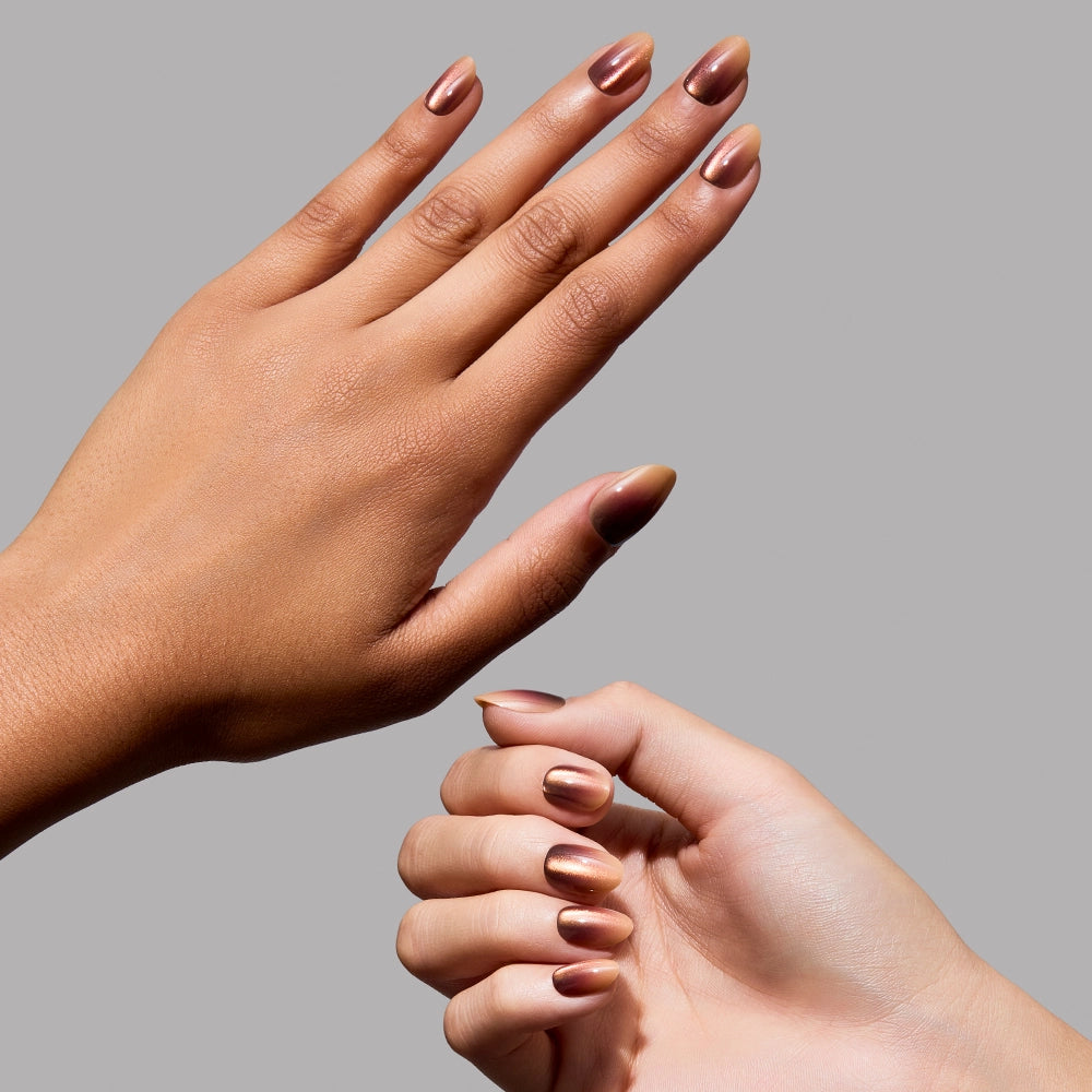 Two hands with brown, almond-shaped nails painted in glamnetic’s “Bitter Orange” metallic gradient polish are shown against a plain gray background. The nails have a glossy, reflective finish reminiscent of a short oval press-on style. - Product image