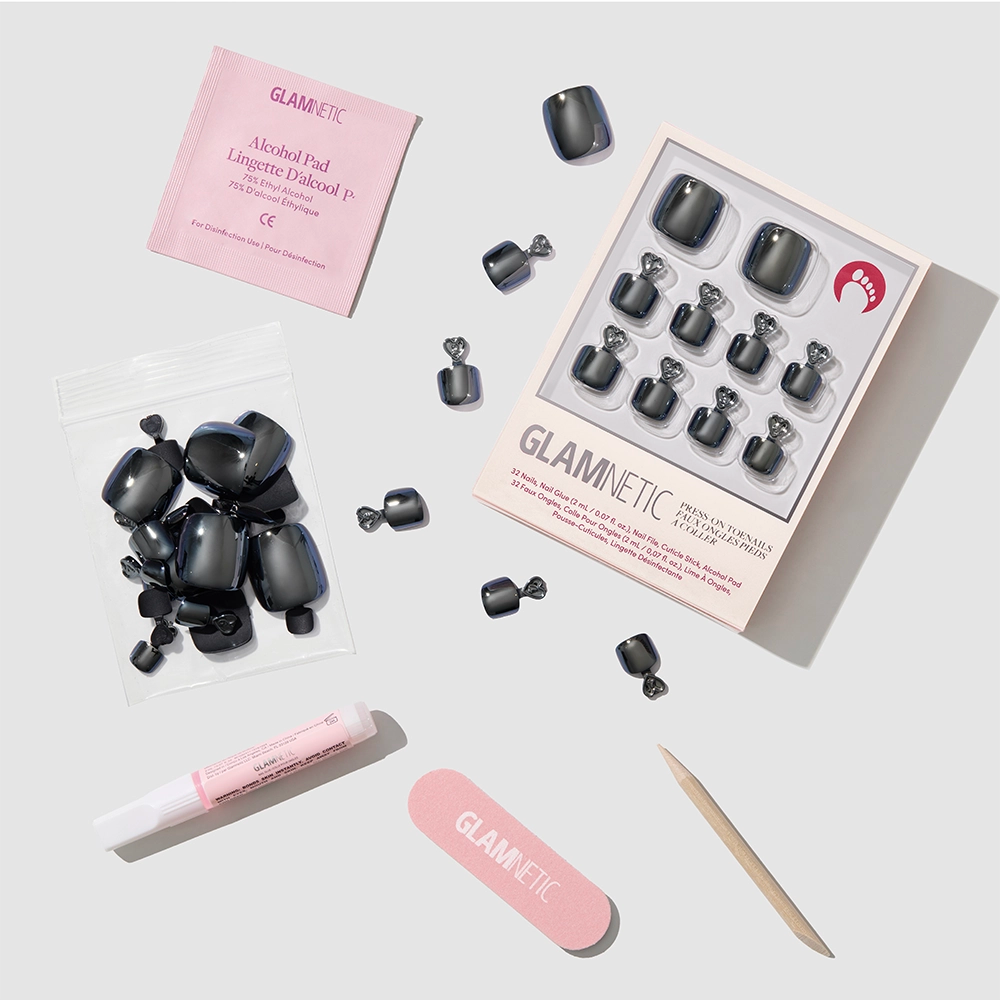 The glamnetic Boba Toenail set includes vegan glossy black press-on nails, nail glue, a wooden cuticle stick, a pink nail file, an alcohol pad, and extra nails—all neatly displayed on a light gray background. - Product image