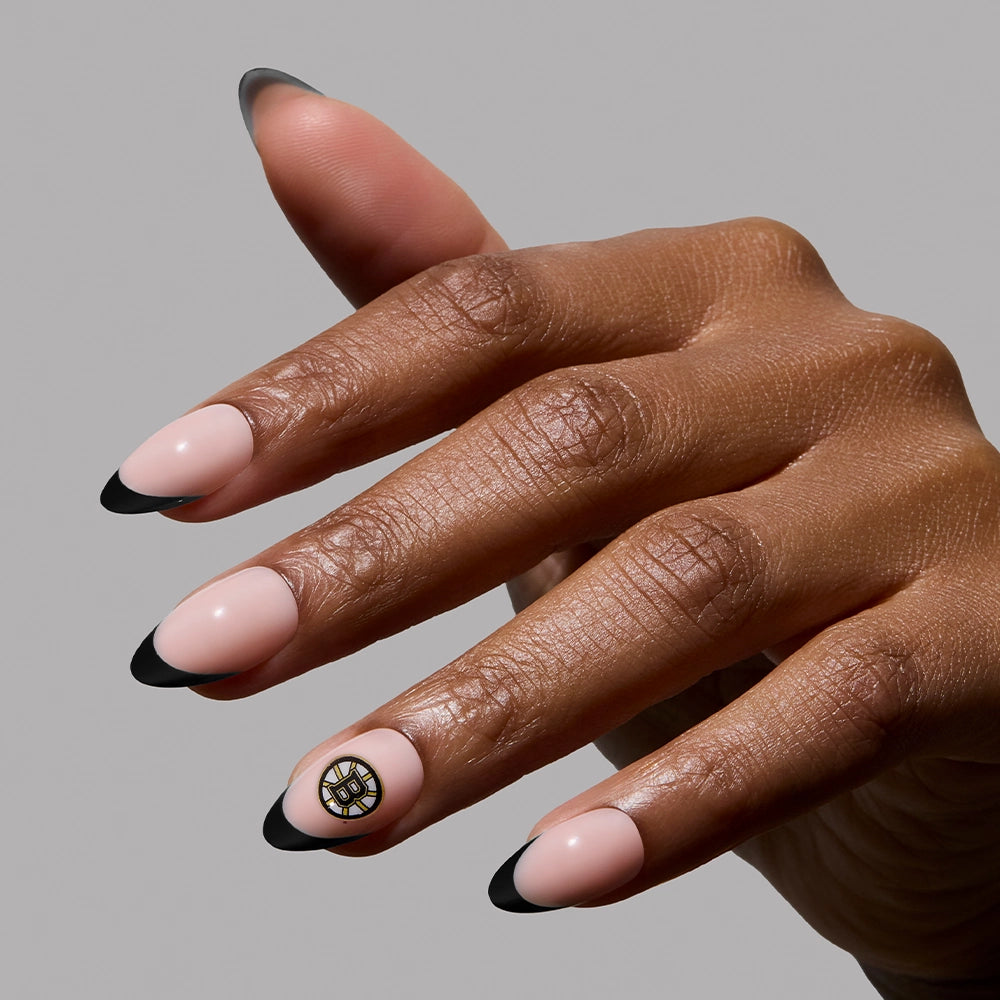 The glamnetic Boston Bruins Press-On Nail Set features medium almond-shaped nails with a nude base, black French tips, and a gold and black circular accent on the ring finger for a subtle fandom look. - Product image