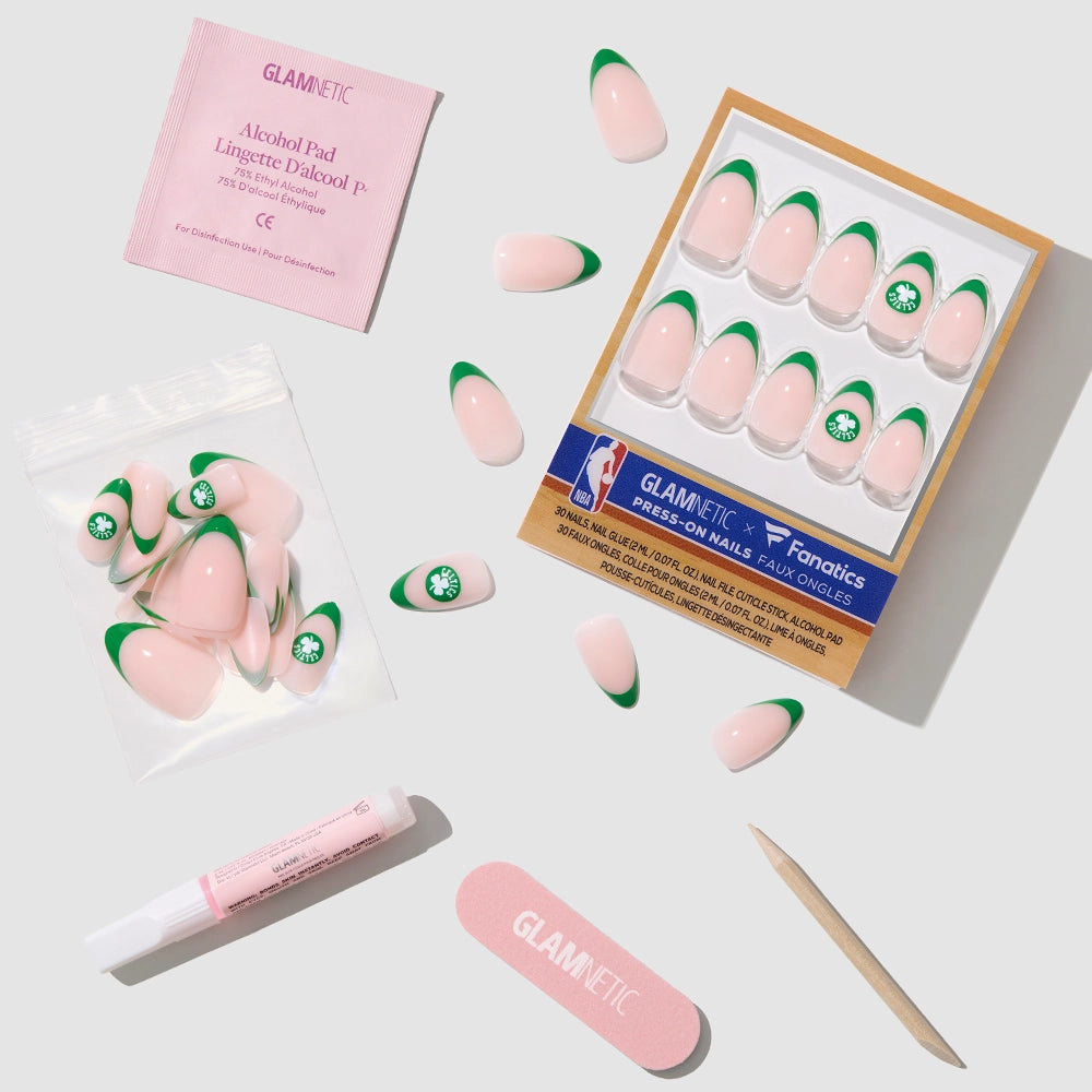 The glamnetic Boston Celtics Press-On Nail Set features pink French tips with green tips and a clover design, plus nail glue, cuticle stick, pink file, alcohol pad, and extra nails—all arranged on a light gray background. - Product image