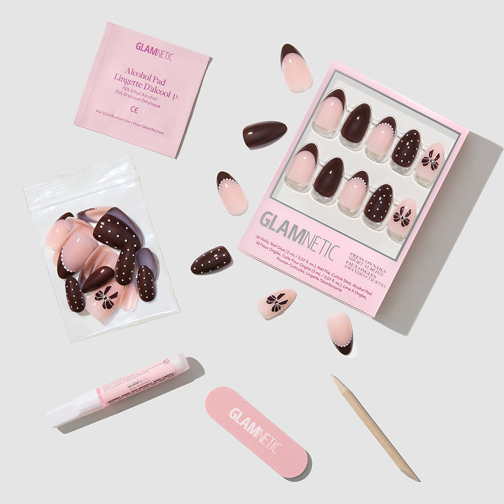 Glamnetic Bow Season short almond press-on nails in chocolate brown and light pink with bow and polka dot patterns, including a storage box, loose nails, nail glue, an alcohol pad, a nail file, and a wooden cuticle pusher. - Product image
