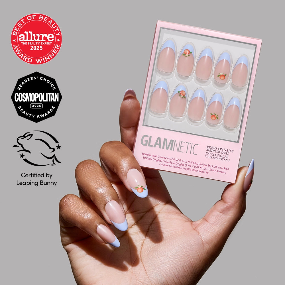 A hand holds a glamnetic Capri Coast Press-On Nail Set with blue French tips and flower accents. Allure, Cosmopolitan, and Leaping Bunny badges certify this salon-quality mani shown on the left.