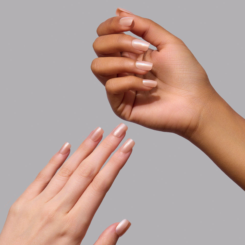 Two hands featuring short, squoval Glamnetic Champagne Veil press-on nails with a glossy, pale pink pearl chrome finish. - Product image