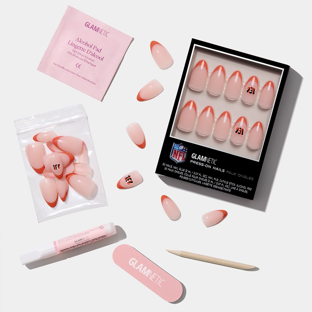 The glamnetic Cincinnati Bengals Press-On Nail Set features pink press-ons with red tips, some numbered, arranged with a nail file, cuticle stick, glue, alcohol pad, and extra loose nails on a white background. - Product image