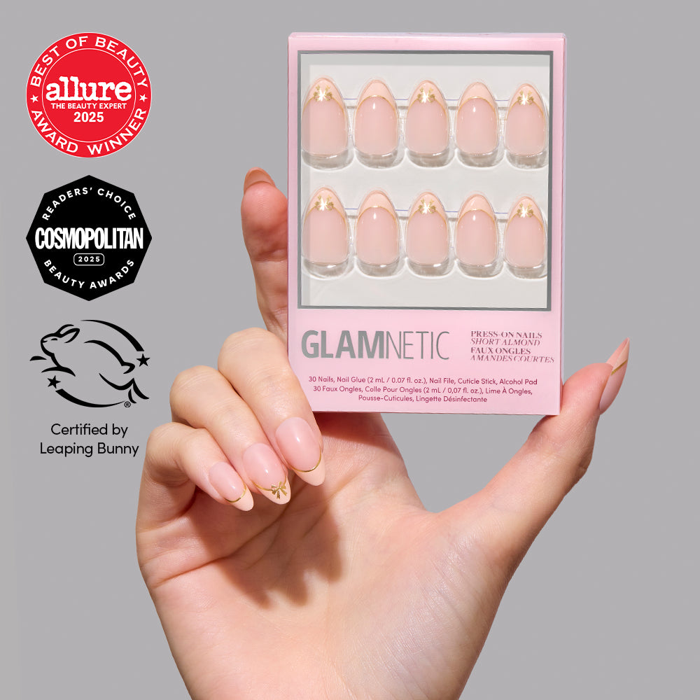 Hand holding a box of Cindy Lou glamnetic short almond press-on nails with a pink base and gold star design, featuring beauty award seals and a Leaping Bunny vegan certification logo. - Product image