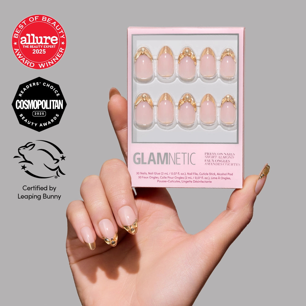 A hand with short almond nails featuring gold French tips holds a box of glamnetic Citrine press-on nails. On the left are beauty award badges and a cruelty-free certification logo.