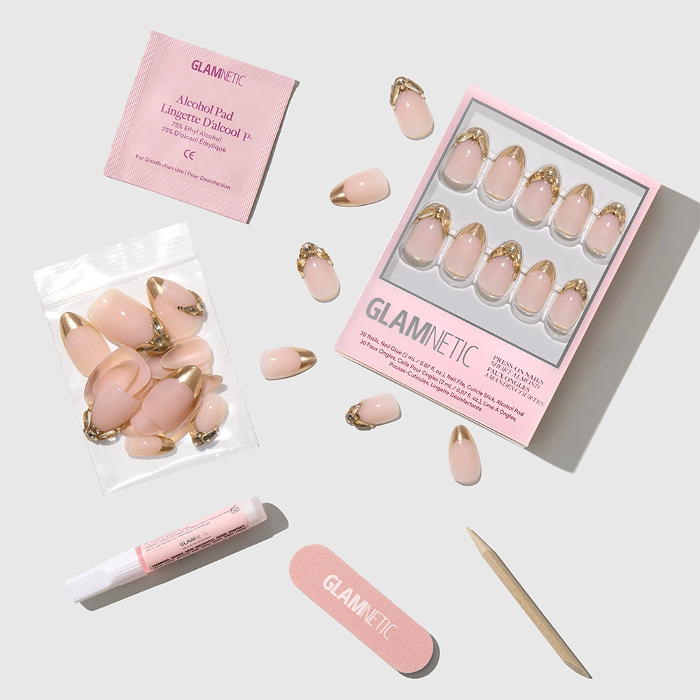 The Glamnetic Citrine set features short almond press-on nails in light pink with gold French tips, displayed with a nail file, cuticle stick, nail glue, alcohol pad, and extra nails on a light gray background. - Product image