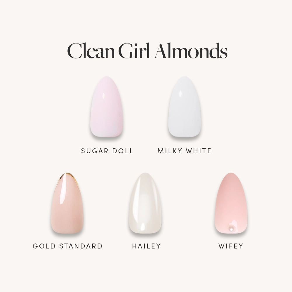 Five short almond press-on nails from glamnetic’s Clean Girl Almonds collection are displayed in a range of shades: light pink (Sugar Doll), white (Milky White), beige (Gold Standard), ivory (Hailey), and pale pink (Wifey)—each labeled beneath for a salon-quality mani.