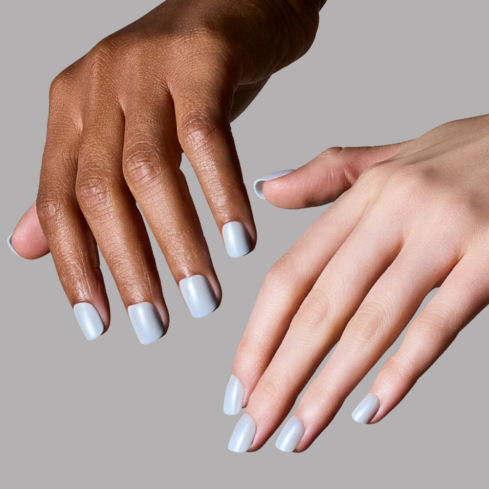 Two hands—one with a light skin tone and one with a dark skin tone—wear the salon-quality Clear Skies short press-on nails by glamnetic in light blue, shown against a plain gray background. - Product image