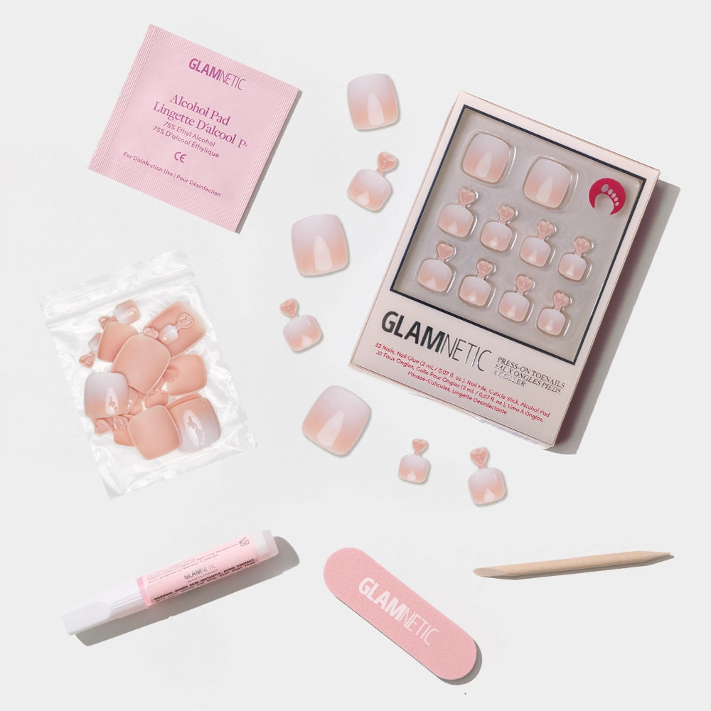 A flat-lay of the Glamnetic nude ombré press-on toenail kit with a white fade and full nail care accessories. - Product image