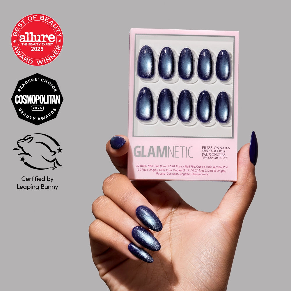 A hand with dark blue, medium oval press-on nails featuring a luxurious velvet finish holds a box of Crystal Cantation nails by glamnetic. The gray background showcases beauty and cruelty-free certification badges on the left. - Product image