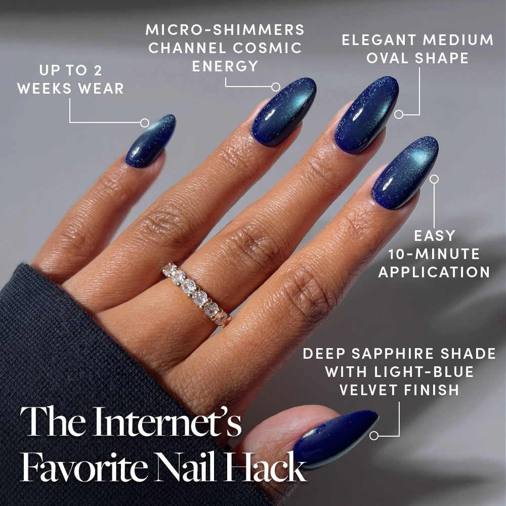 A hand displays glamnetic’s Crystal Cantation press-on nails in a medium oval shape, featuring deep sapphire-blue color with micro-shimmers and a velvet finish. The image highlights benefits such as 2 weeks of wear, 10-minute application, an elegant silhouette, and a unique cosmic energy effect. A gold ring adorns one finger. These nails offer a luxurious look with effortless style. - Product image