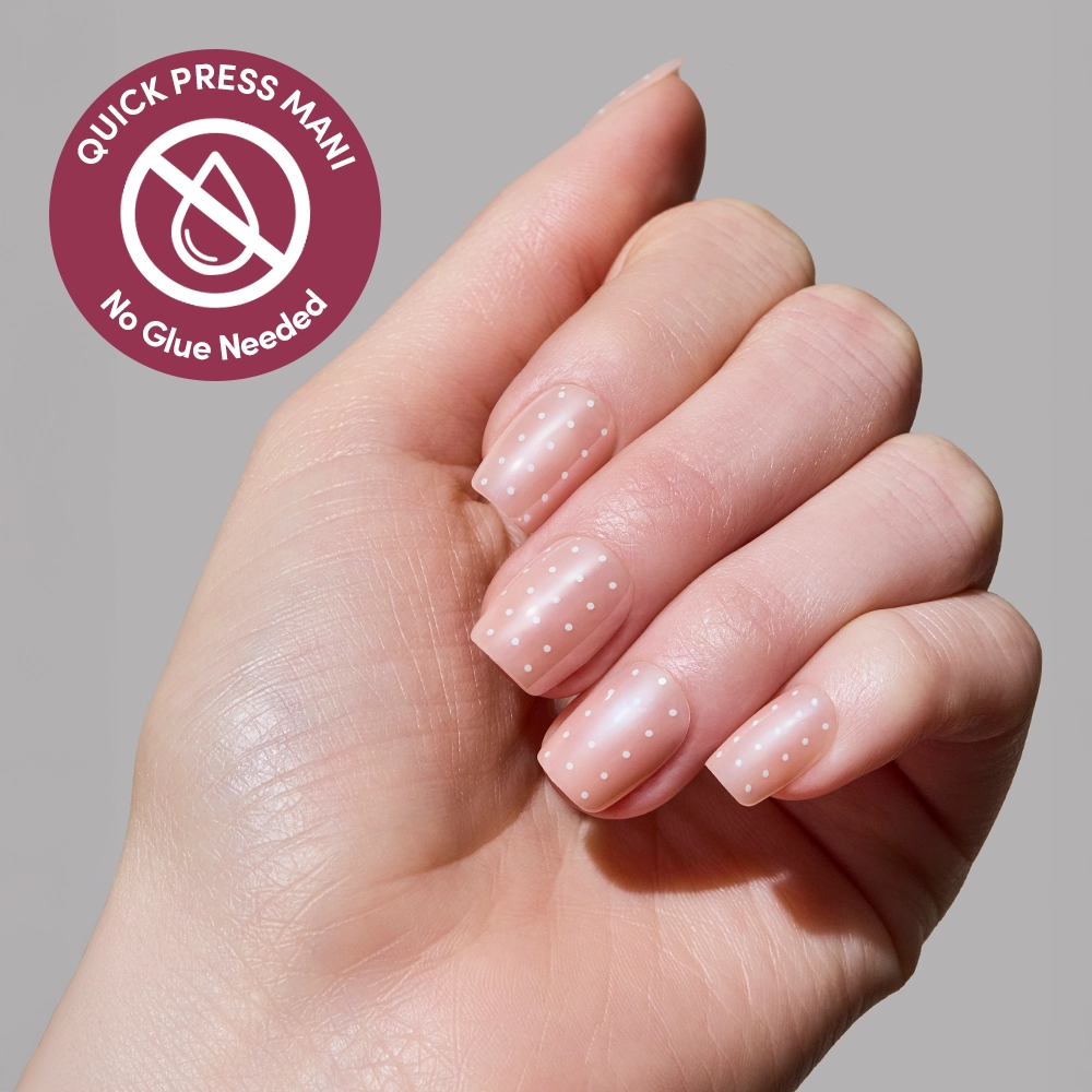 A hand with neatly manicured glamnetic Dainty Dots press-on nails features pale pink polish with white polka dots. A badge reads “Quick Press Mani, No Glue Needed” against a plain light gray background. - Product image