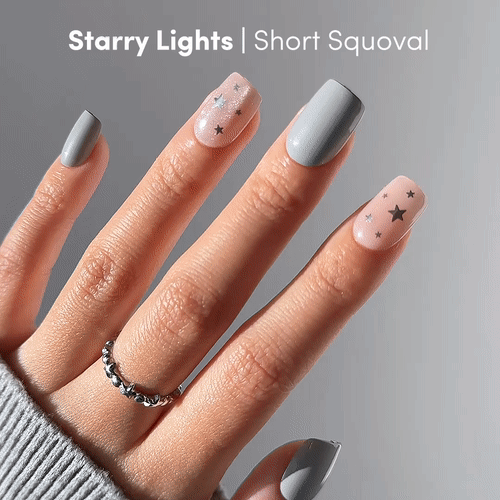 A hand models glamnetic Starry Lights short squoval nails: three with a gray velvet finish, two nude with black stars. Shown with a silver ring and gray sweater. Text: Starry Lights | Short Squoval.