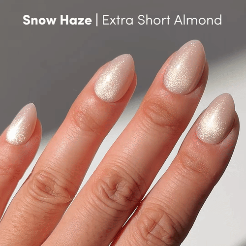 A hand with extra short almond glamnetic Snow Haze press ons in a shimmery pale white, shown against a neutral background to highlight their glossy, velvet finish.