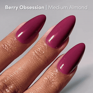 A close-up shows a hand with medium almond-shaped glamnetic press-on nails in a glossy berry shade called Berry Kiss. The text at the top reads, Berry Kiss | Medium Almond.