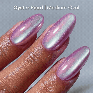 A hand with medium almond-shaped nails painted in glamnetic’s Timeless Oyster, a shimmery pearlescent pink and silver shade, against a light gray background.