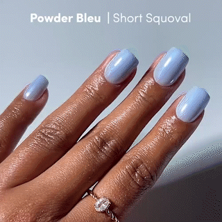 A hand with neatly manicured glamnetic Powder Bleu press-on nails, featuring a light powder blue shade in a short squoval shape. The person is also wearing a silver ring adorned with a clear gemstone. - Product image