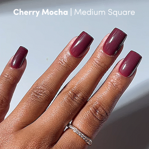 A hand with medium square-shaped nails painted in glamnetic’s Cherry Mocha, a glossy, cruelty-free shade, and wearing a thin diamond-studded ring on the ring finger. - Product image