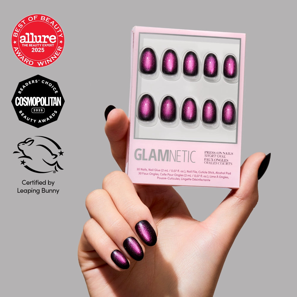 Hand holding Glamnetic Dark Romance short oval press-on nails in black with a pink cat-eye shimmer and a luxe velvet finish. Awards shown: Allure Best of Beauty 2025, Cosmopolitan 2025, Leaping Bunny certified.