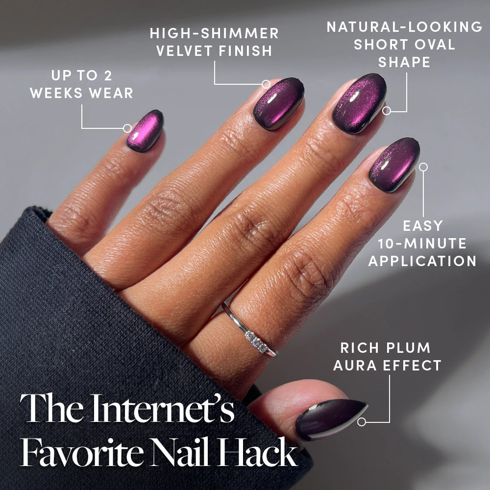 A hand with short, oval, plum-colored glamnetic Dark Romance press-on nails featuring a high-shimmer velvet finish and wearing a simple ring. Text highlights the nails’ 2-week wear, easy 10-minute application, and rich aura effect. - Product image