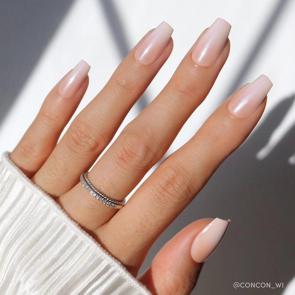 A hand with long, coffin-shaped nails in the pale pink “Delicate Touch” by glamnetic and two silver rings on the ring finger, wearing a white ribbed sleeve. - Product image