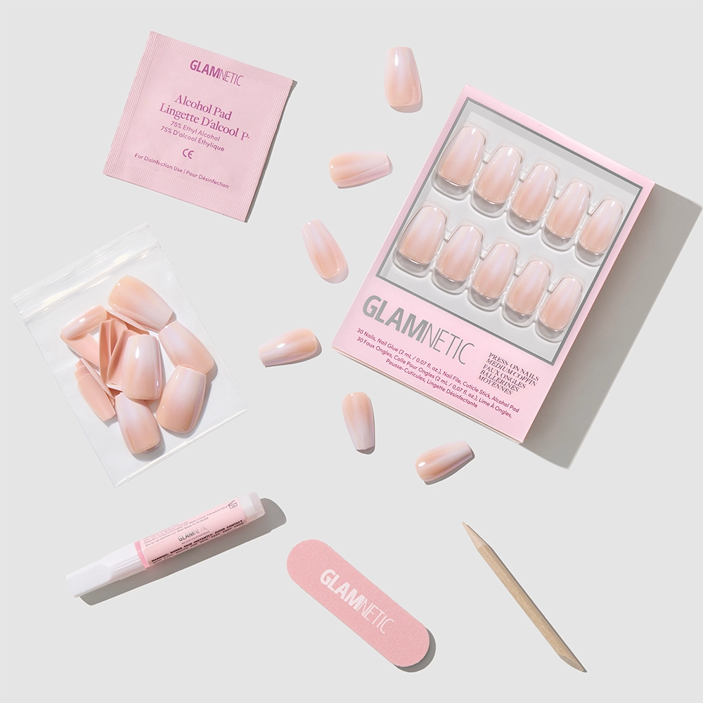 Delicate Touch by glamnetic: light pink coffin-shaped press-on nails, plus alcohol pad, nail file, cuticle stick, glue, and extra nails—all arranged on a white background with glamnetic packaging. - Product image