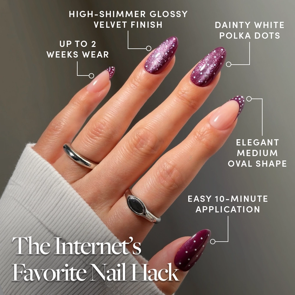 A hand adorned with oval-shaped, glossy purple Dotted Mulberry nails from glamnetic—featuring eye-catching glitter and delicate white polka dots—displays our press-on nail set. The text emphasizes 2 weeks of wear, a quick 10-minute application, high shimmer, an elegant oval shape, and dainty nail art. Three silver rings on the hand add an extra touch of style. - Product image