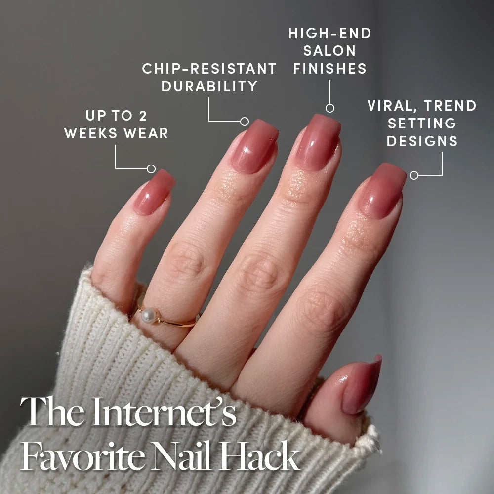 A hand with long, semi-transparent glossy nails in the chic “Dusty Pink” shade by glamnetic is shown. The pinkish-mauve nails feature a salon-quality finish and showcase chip-resistant durability, viral designs, and up to 2 weeks of wear. The person is accessorized with a beige sweater and a gold ring. - Product image