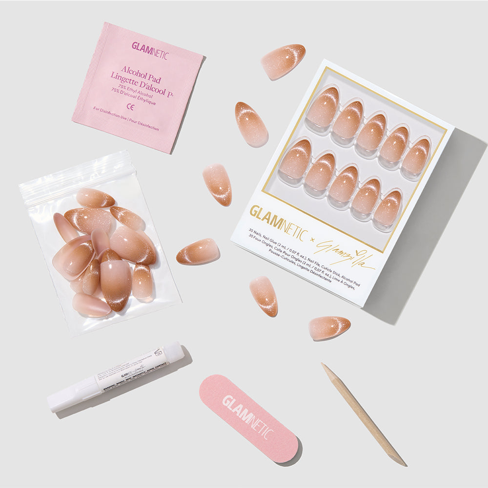 A flat lay of the glamnetic EARNED NOT GIVEN press-on nails kit displays short almond ombré pink nails, extra nude nails in a bag, alcohol pad, nail file, cuticle stick, and glue—all neatly arranged on a white surface. - Product image
