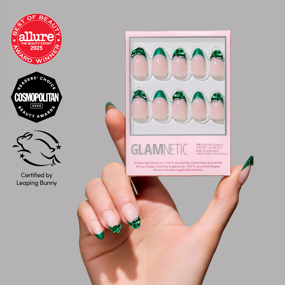 A hand with green French tip nails holds a box of glamnetic Emerald press-on nails with a matching design. Allure and Cosmopolitan beauty award logos and a Leaping Bunny cruelty-free certification appear beside the box.