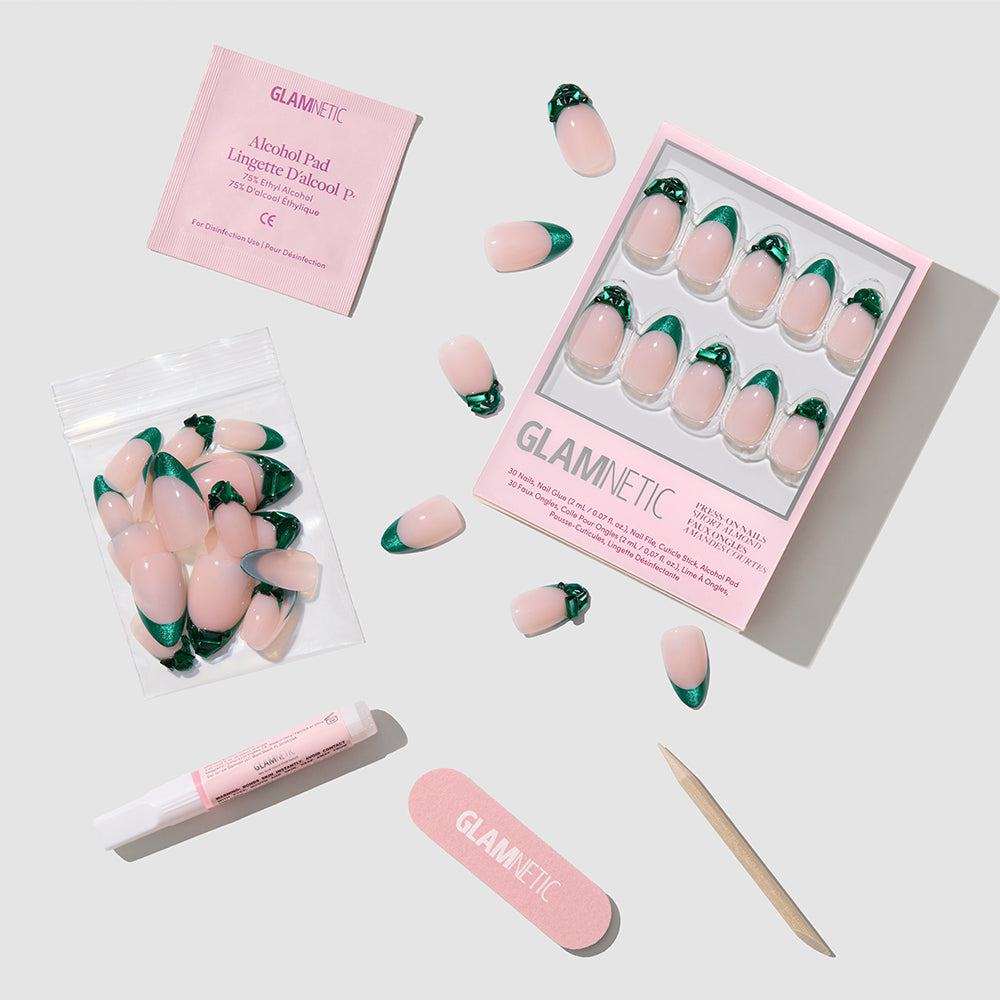 A flat lay of the glamnetic Emerald press-on nails kit, featuring salon-quality pink and green nails in a tray and bag, plus an alcohol pad, nail glue, nail file, wooden cuticle stick, and loose nails on a light background. - Product image
