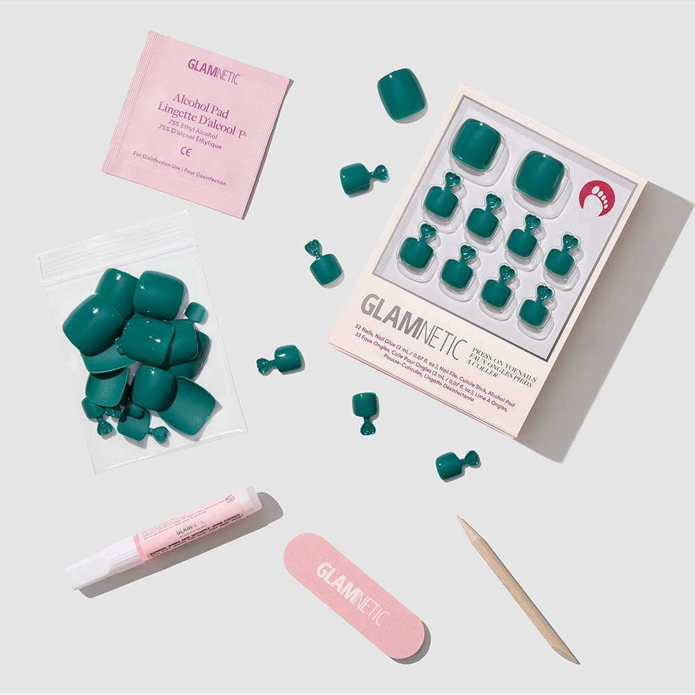 The glamnetic Emerald Green Toenail set includes press-on toenails, a pink nail file, wooden cuticle stick, nail glue, alcohol pad, and extra nails, all neatly arranged on a light background. - Product image