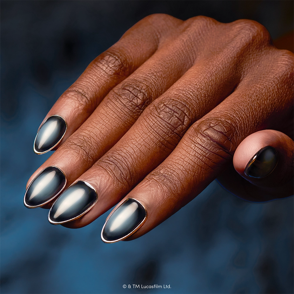 A hand with metallic, silver-tipped, almond-shaped cruelty-free nails in “Emperor” by glamnetic and a matching thumb ring is shown against a dark, blurred background. - Product image