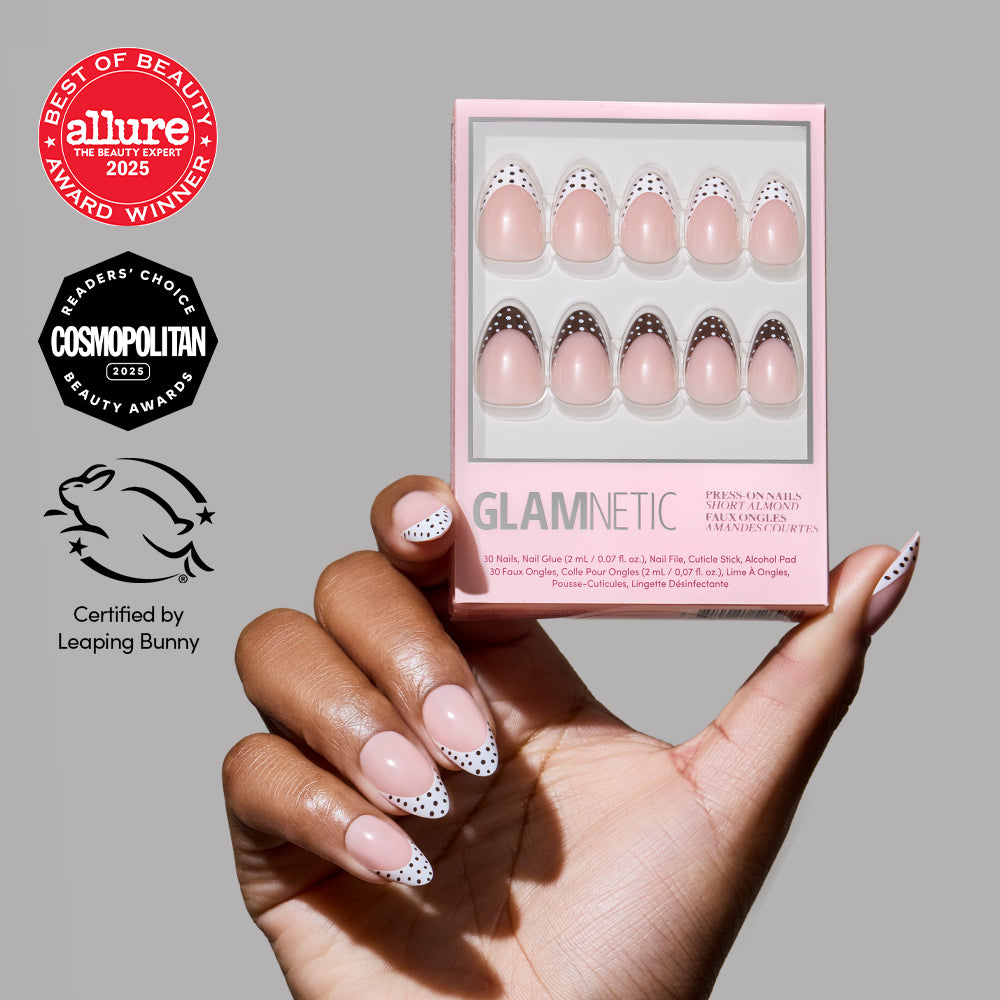 A hand with pink short almond "Polka In Positano" press-on nails by glamnetic, featuring black and white polka dot tips, holds a glamnetic nail set box. Award badges and a Leaping Bunny cruelty-free certification appear on the left.