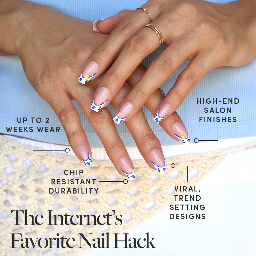 A woman with manicured medium coffin nails featuring blue and yellow floral mosaic French tips (Tuscan Twist by glamnetic) rests them on crocheted fabric. Enjoy trendy, salon-quality press-ons with up to two weeks’ long-lasting wear. - Product image