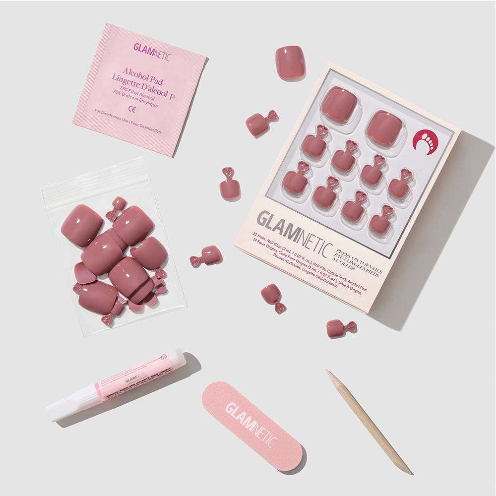 The glamnetic Fall Mauve Toenail set includes press-on toenails with glue, a cuticle stick, nail file, alcohol pad, and extra nails, all neatly displayed on a light surface. - Product image