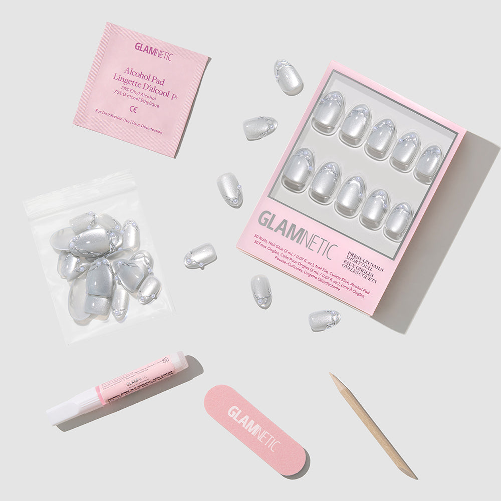 A set of Fine Silver short oval press-on nails by Glamnetic in a box, including a nail file, nail glue, an alcohol pad, a cuticle pusher, and a bag of extra nails. - Product image