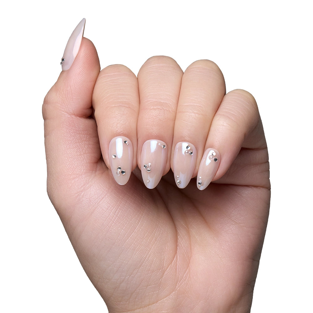 A hand with almond-shaped nails from glamnetics First Dance vegan nail set, painted in a sheer nude and decorated with small silver rhinestones, is shown against a plain white background. - Product image