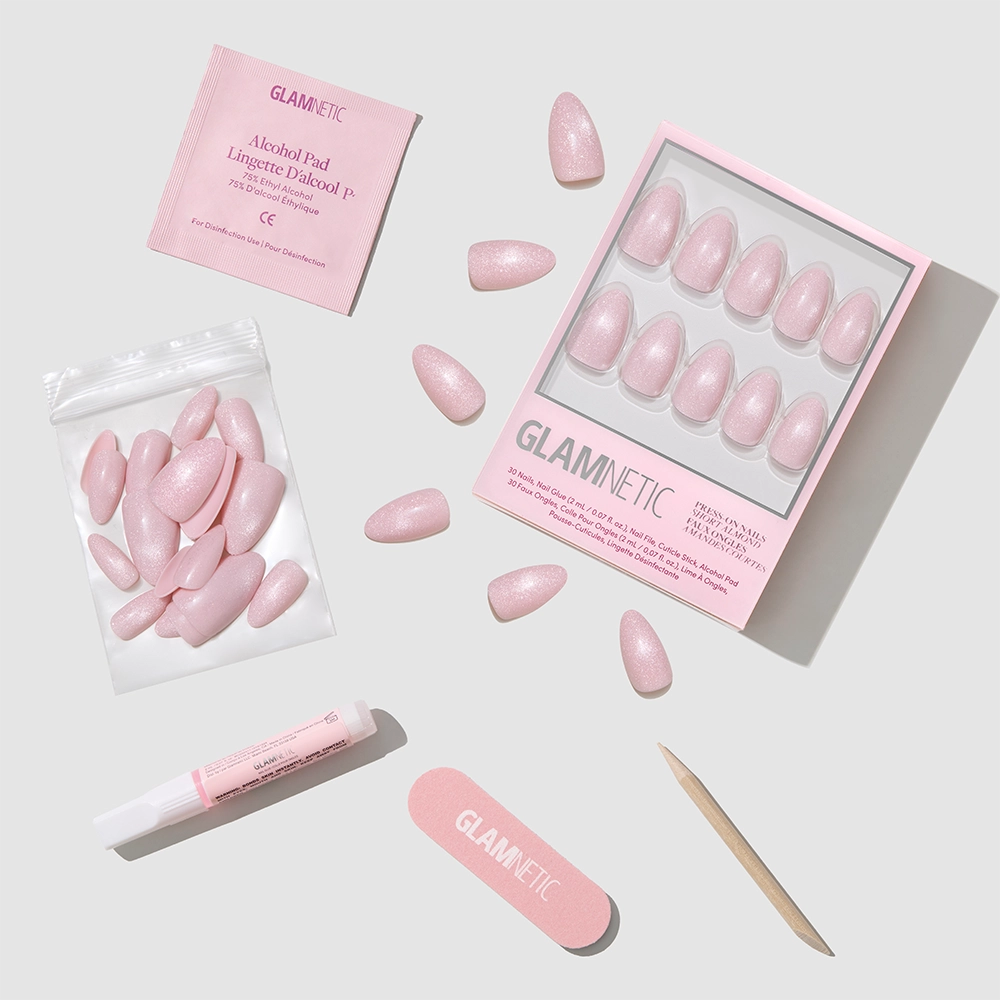 A flat lay of glamnetic’s Forever Pink press-on nails kit, featuring short almond nails, nail file, cuticle stick, glue, alcohol pad, and extra nails—all neatly arranged on a light gray background.