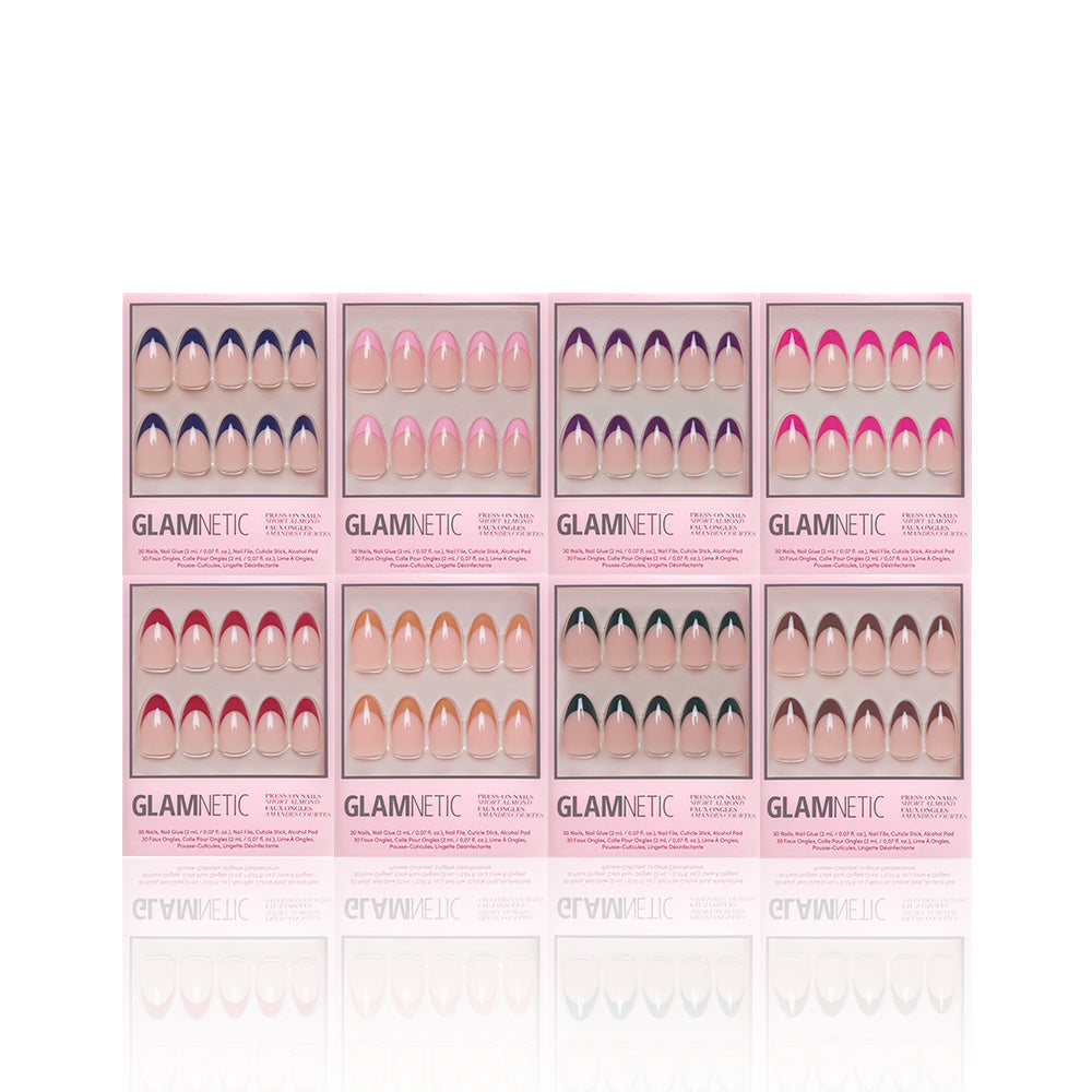 Eight boxes of glamnetic’s French Tip Collection are arranged in two rows, each with a unique short almond nail design in pink, nude, and accent shades. Reusable nails are visible through a clear window on every pink package.