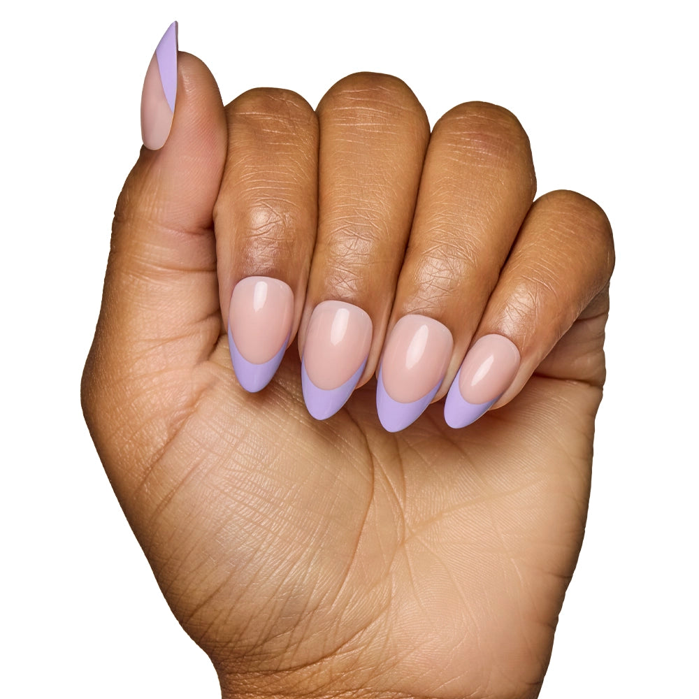 A hand with medium brown skin shows short, almond-shaped nails wearing glamnetic’s French Lilac: a nude base with pastel purple tips, posed against a white background. - Product image