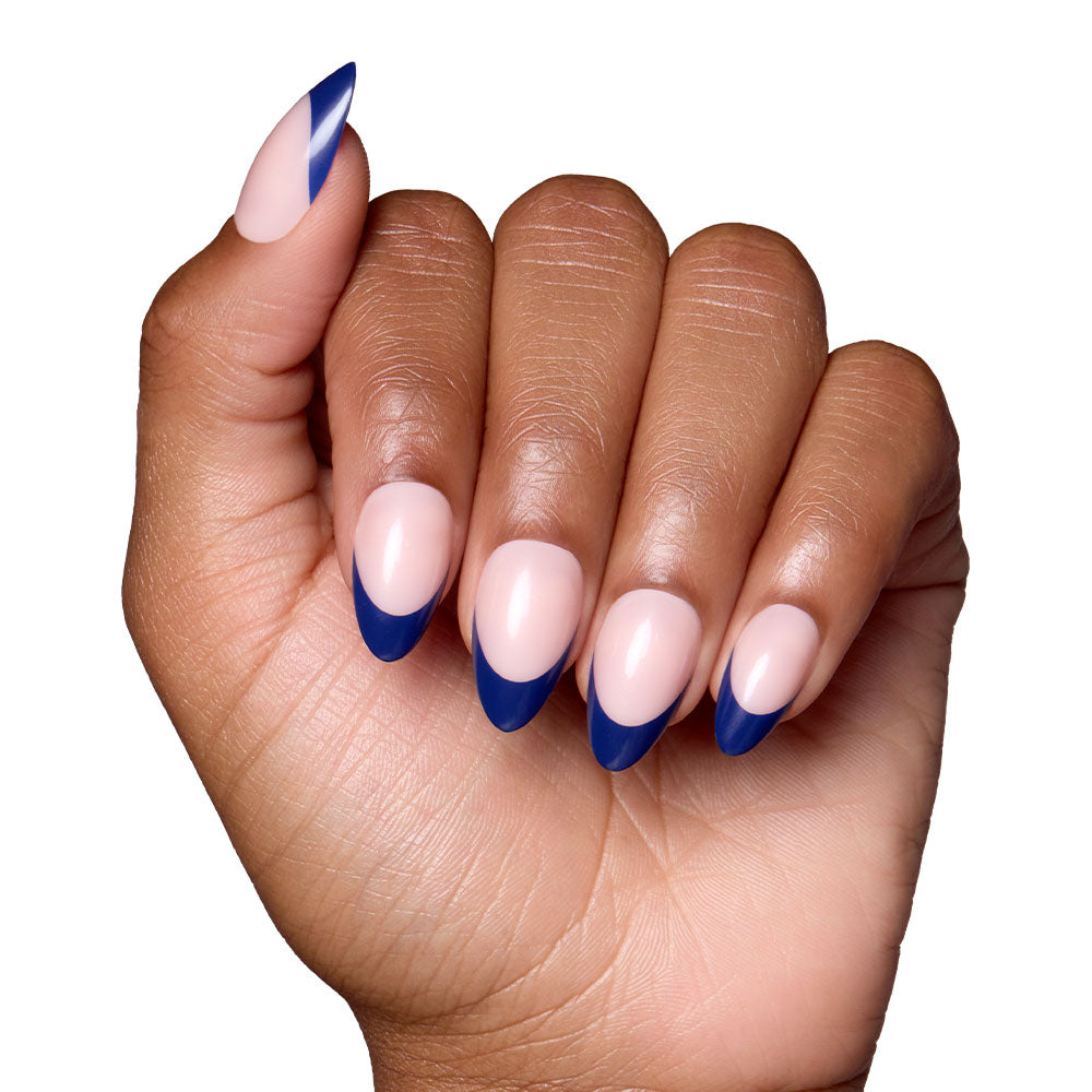 A hand with short almond nails in glamnetics French Riviera—glossy nude base and navy French tips—posed against a white background. - Product image