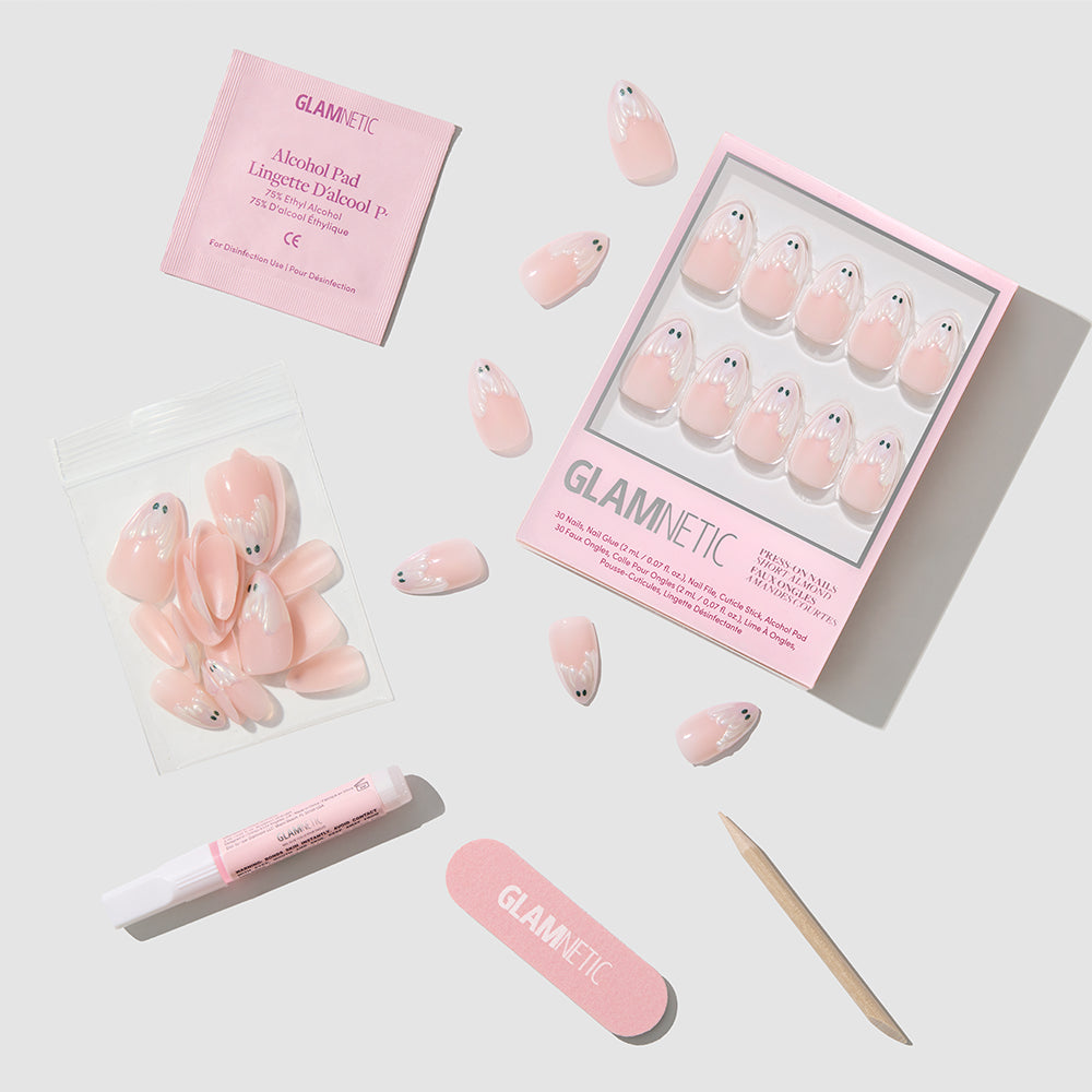 Glamnetic’s “Ghost Besties” set features pink, short almond press-on nails with optional ghost nail art, and includes nail glue, a wooden cuticle stick, a mini nail file, an alcohol pad, plus extra nails—all displayed on a white background. - Product image
