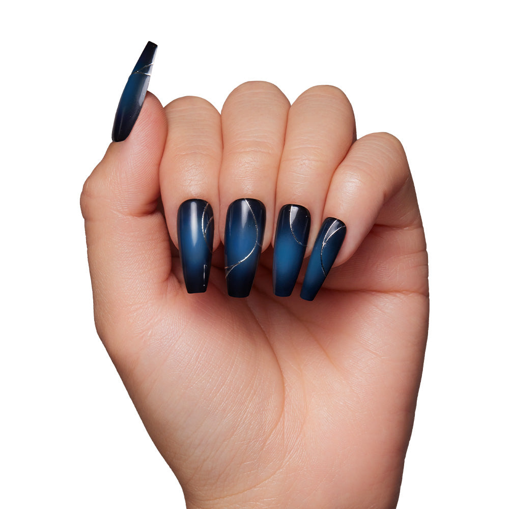 A hand with long, coffin-shaped nails from the glamnetic Ghost House set, featuring a dark blue ombré with thin silver wavy accents, shown against a white background. - Product image